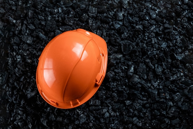 Un casco naranja de un minero yace sobre un montón de carbón, minería de carbón a cielo abierto, copia espacio.