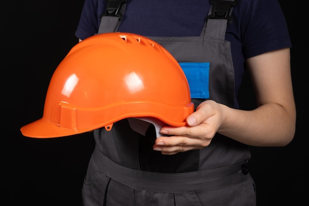 Casco naranja protector en manos de una constructora sobre un fondo negro