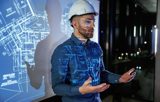 Casco protector en la cabeza El arquitecto con casco fuerte está cerca del proyector con el plan de construcción