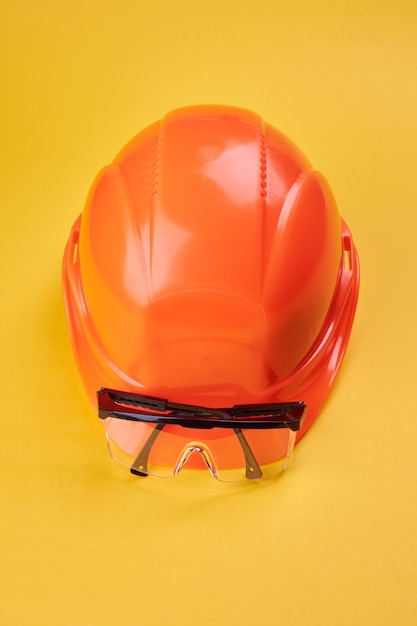 casco protector naranja y gafas de seguridad cerca de él en un amarillo brillante. orientación vertical. ropa de trabajo protectora y concepto de la industria de la construcción