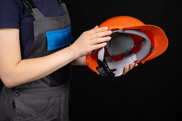 Foto casco protector naranja en manos de una constructora sobre fondo negro