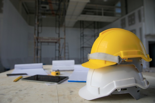 Casco de seguridad blanco y amarillo en el sitio de construcción, andamios en segundo plano.