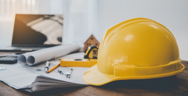 Casco de seguridad casco amarillo colocado en la mesa de trabajo con un plan de diseño de la casa que incluye equipos de ingeniería