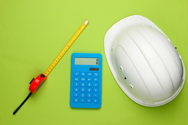 Casco de seguridad de construcción de ingeniería y calculadora, regla en verde. Cálculo del costo de reparación o construcción de una casa. Endecha plana