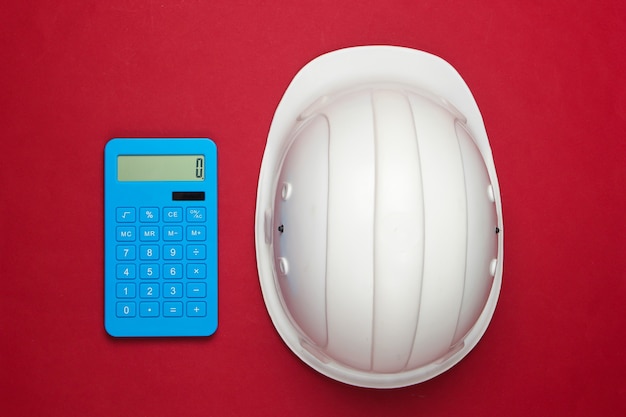 Casco de seguridad de construcción de ingeniería y calculadora en rojo. Cálculo del costo de reparación o construcción de una casa. Endecha plana