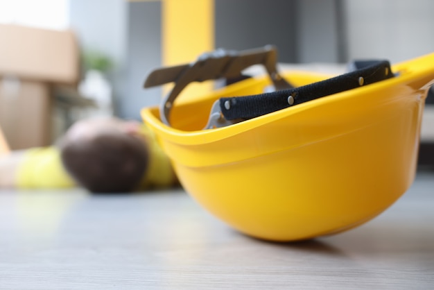 Casco de trabajador amarillo en el piso junto al trabajador de la construcción inmóvil