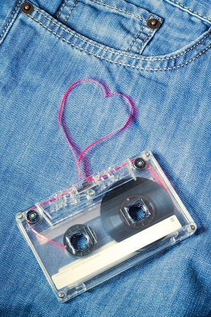 Casete de audio vintage en blue jeans con cinta roja sacada como forma de corazón