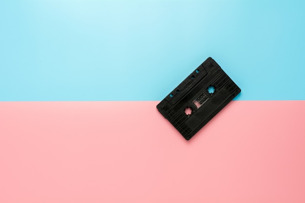 Casete de cinta negro en fondo azul y rosado.