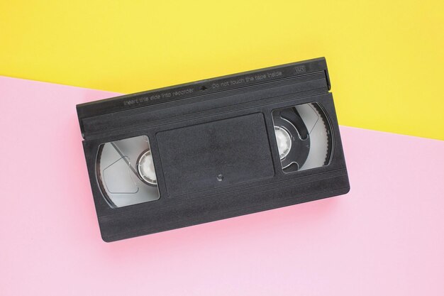 Casete de cinta de vídeo VHS negro sobre fondo amarillo y rosa. Vieja tecnología obsoleta para grabación de cinta