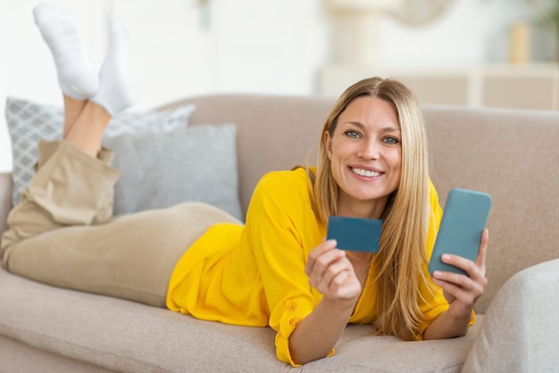 Cashback para mujer rubia caucásica milenaria sonriente adicta a las compras en ropa amarilla con crédito