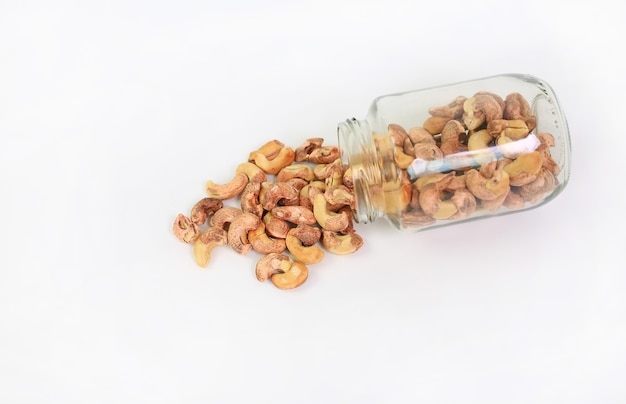 Cashew-Nüsse mit Schale gießen aus Glasflasche isoliert auf weißem Hintergrund. Ansicht von oben