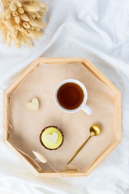 Cashewkuchen mit einer Tasse Tee auf einem Tablett mit getrockneten Blumen auf dem Bett