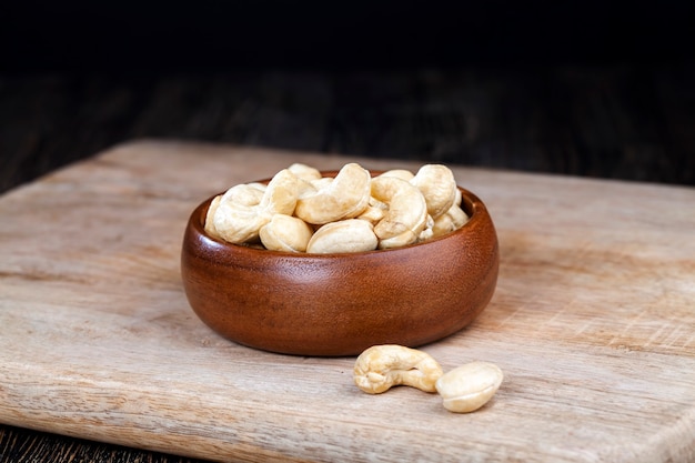 Cashewnüsse auf einem alten Holztisch und in einer Holzschale, Nahaufnahme einer großen Anzahl von Cashewnüssen auf einem Tisch und auf einer Holzoberfläche in einer Holzplatte