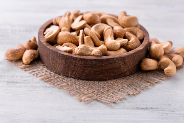 Foto cashewnüsse in der braunen holzplatte auf dem sackleinen auf dem weißen holztischkatalog