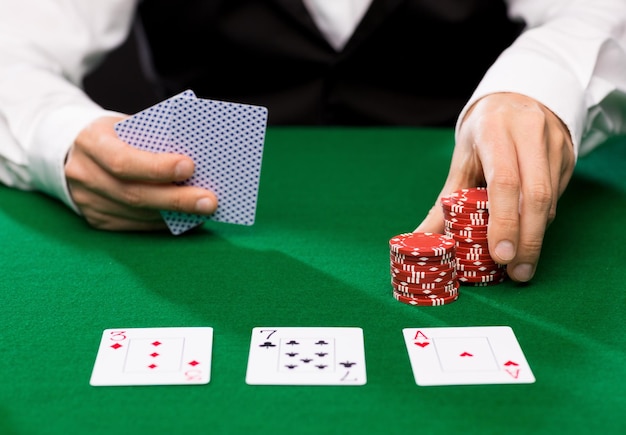 Casino, Glücksspiel, Poker, Menschen und Unterhaltungskonzept - Nahaufnahme des Holdem-Händlers mit Spielkarten und Chips am grünen Tisch