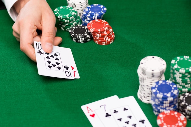 Casino, Glücksspiel, Poker, Menschen und Unterhaltungskonzept - Nahaufnahme eines Pokerspielers mit Spielkarten und Chips am grünen Casino-Tisch