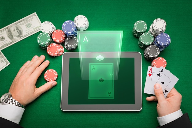 Casino-, Online-Glücksspiel-, Technologie- und People-Konzept - Nahaufnahme eines Pokerspielers mit Spielkarten, Tablet-PC-Computer und Chips am grünen Casino-Tisch