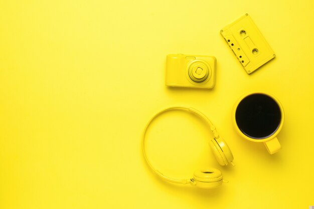 Cassete amarela, fones de ouvido, câmera e caneca de café em um fundo amarelo. tendência de cores. acessórios elegantes. lugar para texto.