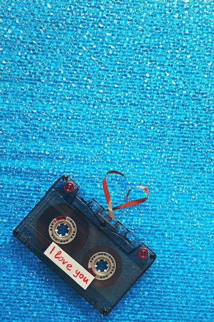 Cassete de áudio retrô com fita em forma de coração no plano de fundo texturizado azul