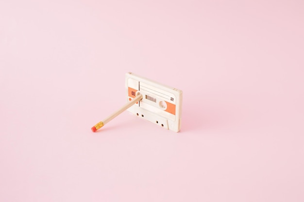 Cassete de áudio retrô com lápis preso em um carretel no fundo rosa