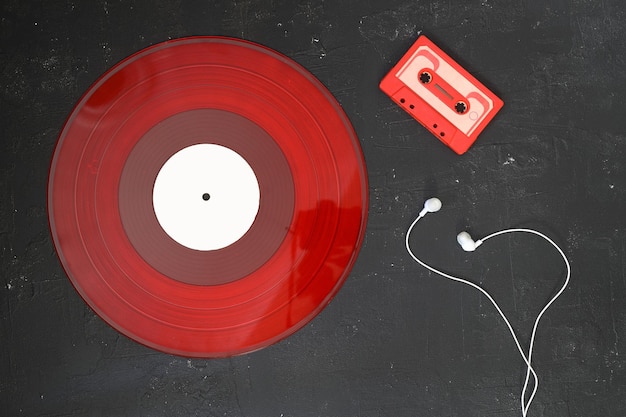 Cassete de áudio vermelho e disco de vinil vermelho em fundo preto estilo retro vista superior com fones de ouvido brancos