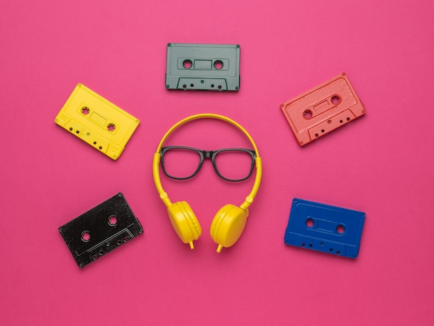 Cassetes de fita multicoloridas, fones de ouvido amarelos e óculos pretos clássicos em um fundo vermelho. Estilo vintage na gravação de som.