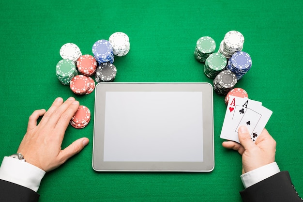 cassino, jogo online, tecnologia e conceito de pessoas - close-up do jogador de pôquer com cartas de baralho, computador tablet pc e fichas na mesa de cassino verde