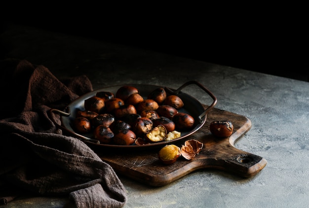 Castañas al horno, fritas en el fondo gris oscuro, listas para comer, copie el espacio