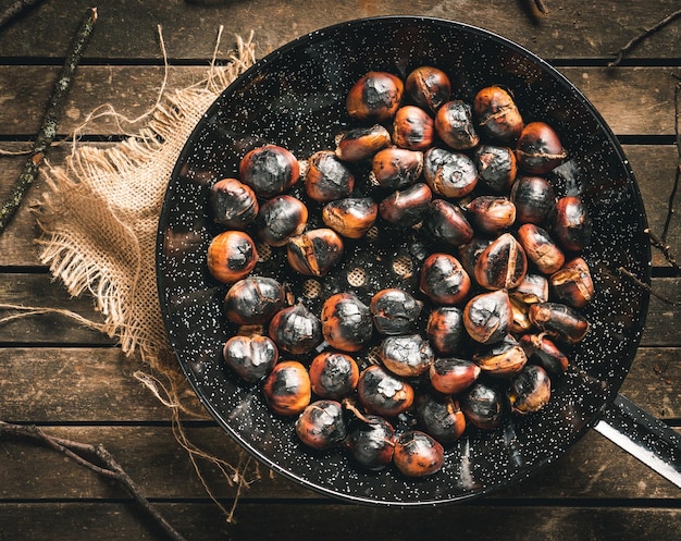 Foto castañas asadas en una sartén de castañas con agujeros en una mesa de madera marrón envejecida