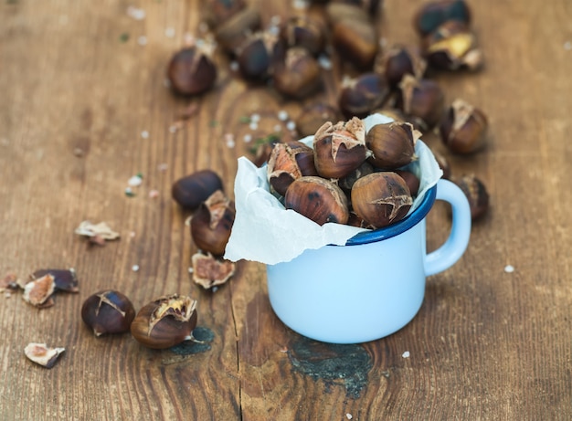 Castañas asadas en taza azul del esmalte en madera rústica, foco selectivo.