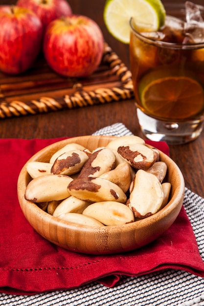 Castanha do Brasil em uma mesa de madeira com maçãs e chá gelado no fundo.