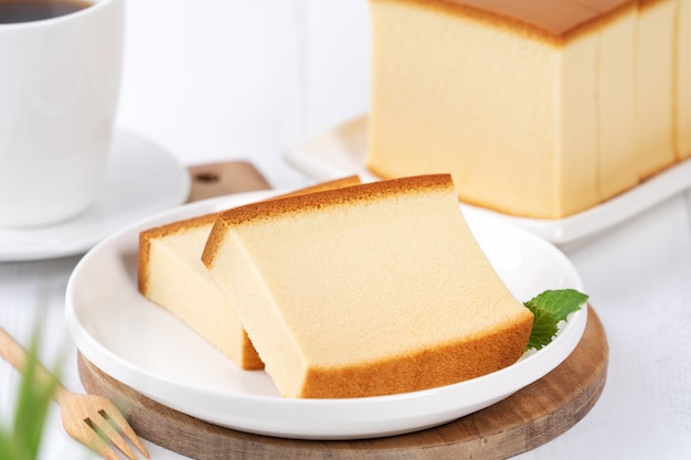 Castella (kasutera) - Linda deliciosa comida japonesa de bolo de esponja em fatias na placa branca sobre a mesa de madeira branca rústica, close-up, copie o conceito de design do espaço.