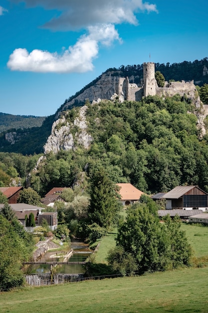 Castelo romântico no topo de uma colina em um vale montanhoso nos Alpes da Suíça, com um céu azul ao fundo, uma pequena vila sob a rocha