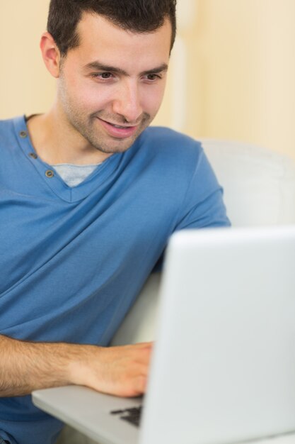 Casual contenido hombre sentado en el sofá usando la computadora portátil