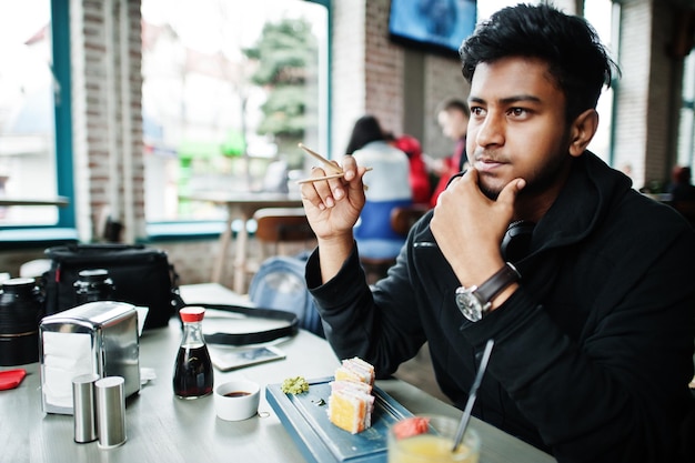 Casual e elegante jovem asiática com fones de ouvido no café comendo sushi