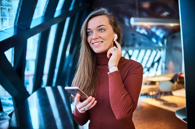 Casual feliz joven mujer morena caucásica con auriculares inalámbricos y teléfono móvil.