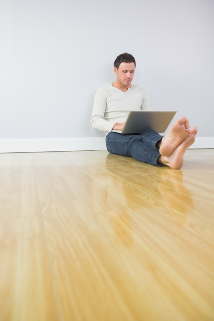 Casual hombre atractivo apoyado contra la pared usando la computadora portátil