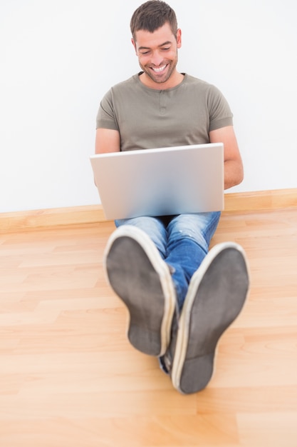 Casual hombre sentado en el piso usando la computadora portátil en casa