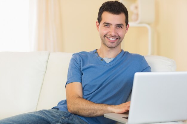 Casual hombre sonriente sentado en el sofá con la computadora portátil