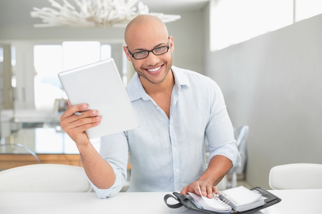 Casual hombre sonriente con tableta digital y diario en casa