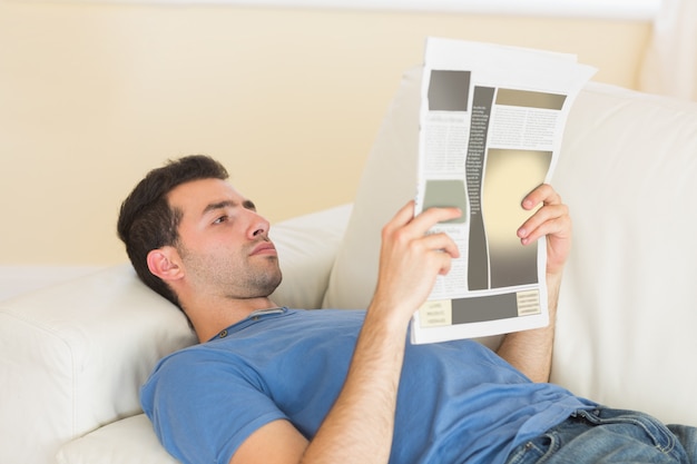 Casual hombre tranquilo acostado en el sofá leyendo el periódico