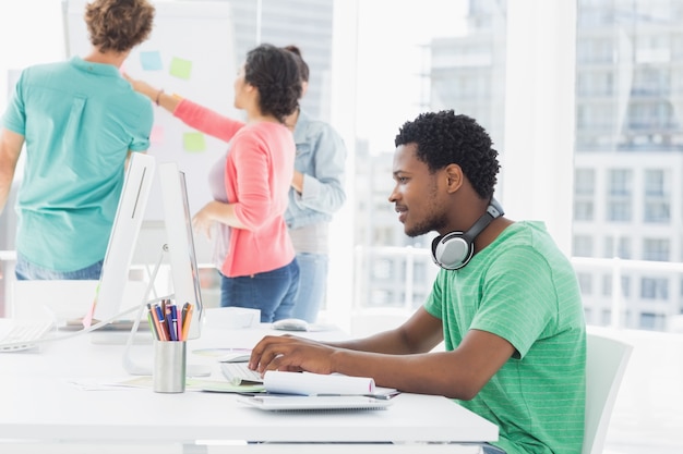 Casual hombre usando la computadora con un grupo de colegas detrás en la oficina