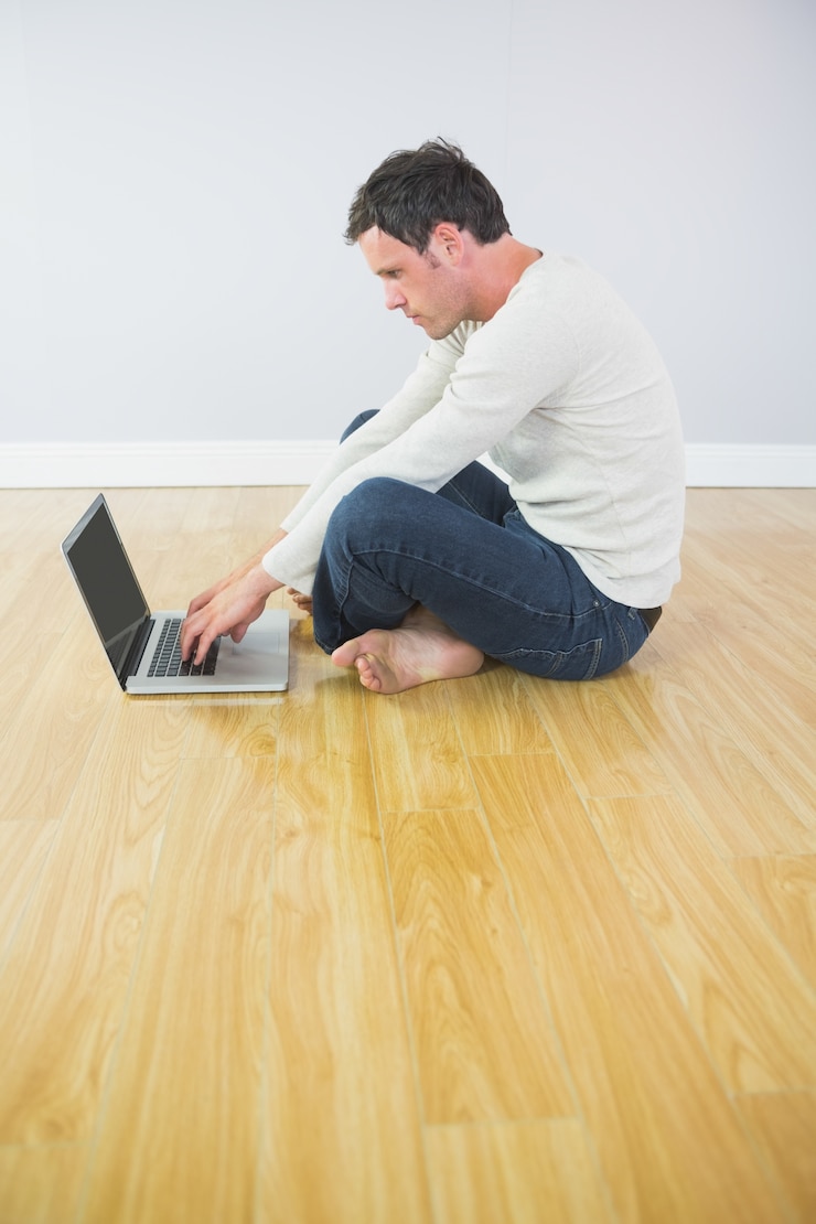 Foto casual homem atraente sentado no chão usando o laptop