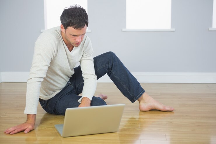 Foto casual, homem bem parecido, sentado no chão usando o laptop