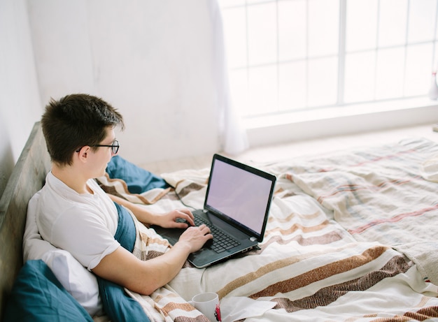 Casual jovem usando o laptop na cama em casa