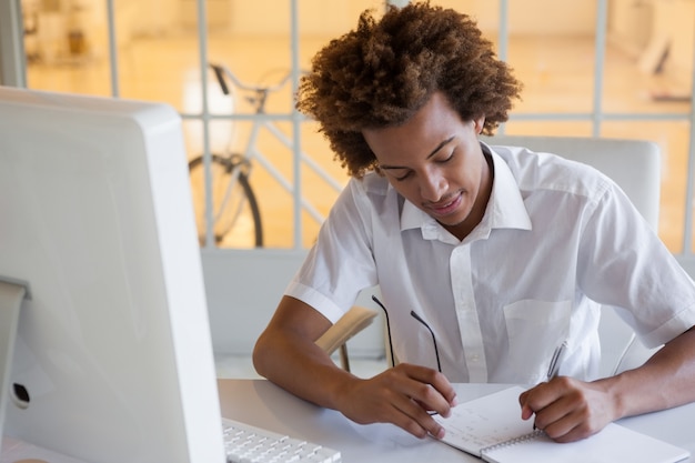 Casual joven empresario escribiendo en su escritorio sonriendo