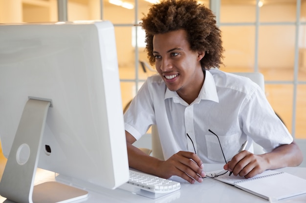 Casual joven empresario sentado en su escritorio sonriendo a la computadora