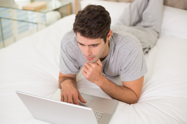 Casual joven usando la computadora portátil en la cama