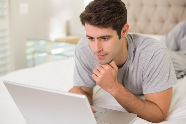 Casual joven usando la computadora portátil en la cama