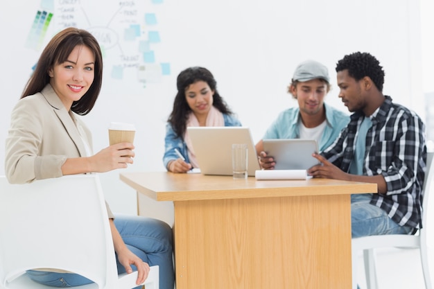 Casual mujer sosteniendo llevar taza de café con colegas detrás en la oficina